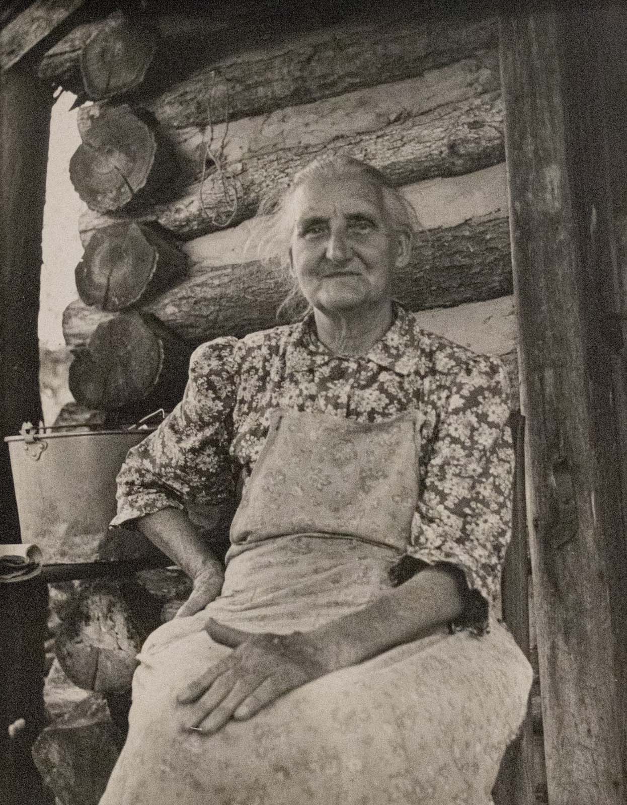 Mrs. J.N. Stufflebeam portrait on a log cabin porch